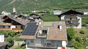 Quartiere residenziale con case dotate di pannelli solari, un campanile e montagne sullo sfondo.
