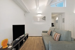 Un salon moderne avec un téléviseur à écran plat, un canapé gris et un plancher en bois.
