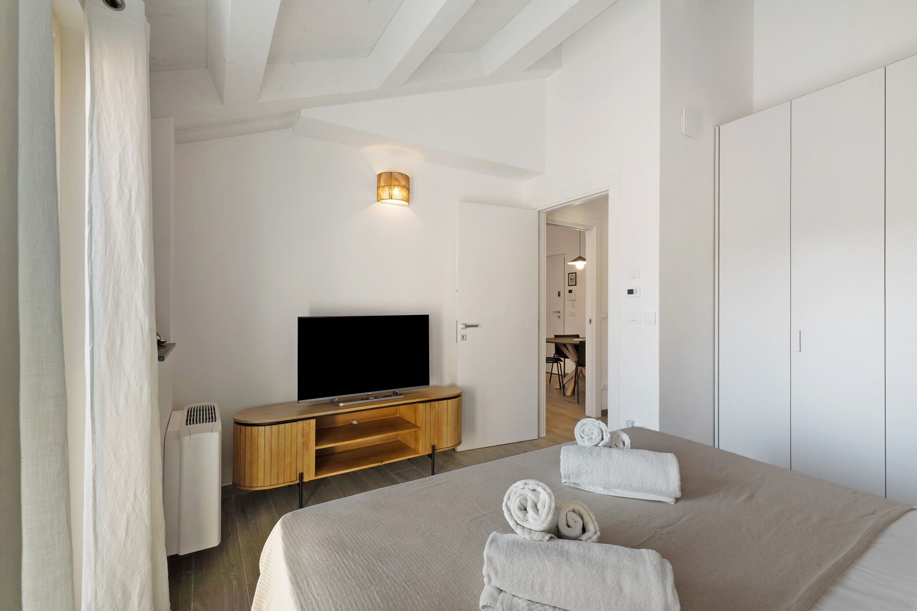 Una habitación de hotel moderna con cama, televisor, mueble de madera y armario.