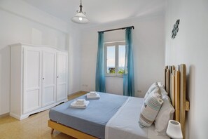 Un dormitorio con cama, armario, ventana con cortinas y vistas al exterior.