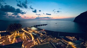 A seaside resort with a beachfront seating area, a pier extending into the water, and a staircase leading to the seating.