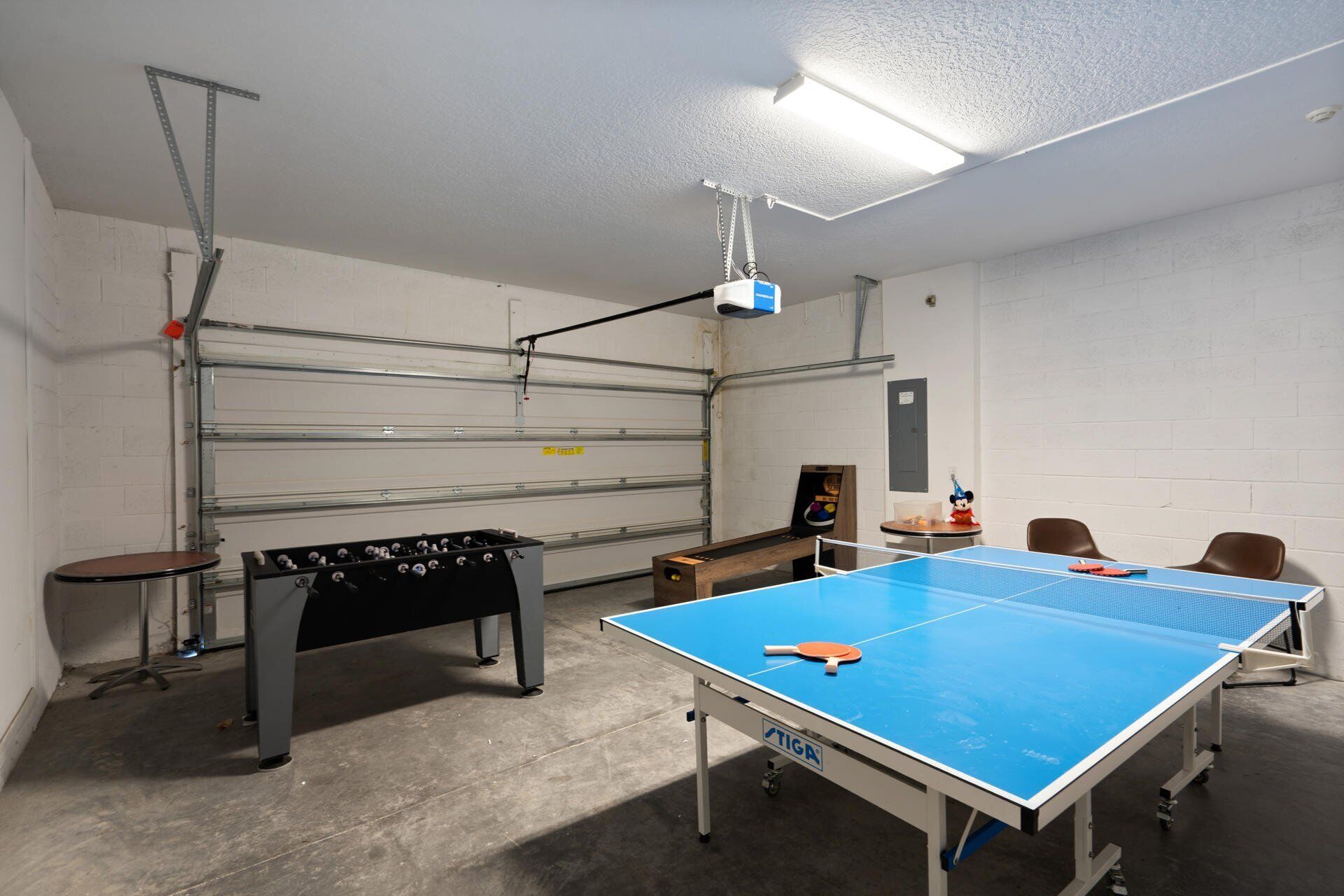 A room with a ping pong table, foosball table, and a projector mounted on the ceiling.