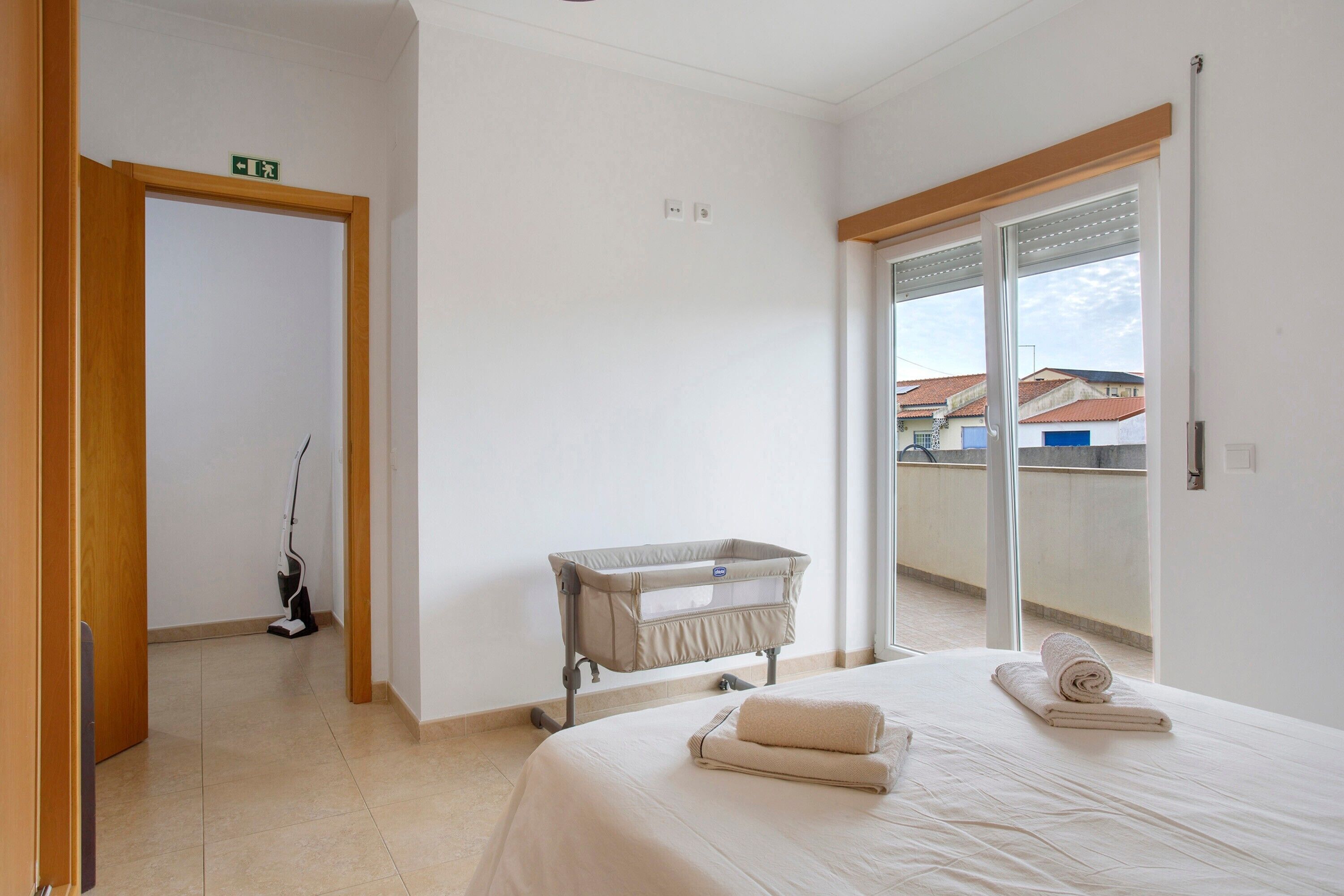 Habitación de hotel con cama, cuna, aspiradora y balcón con vistas.