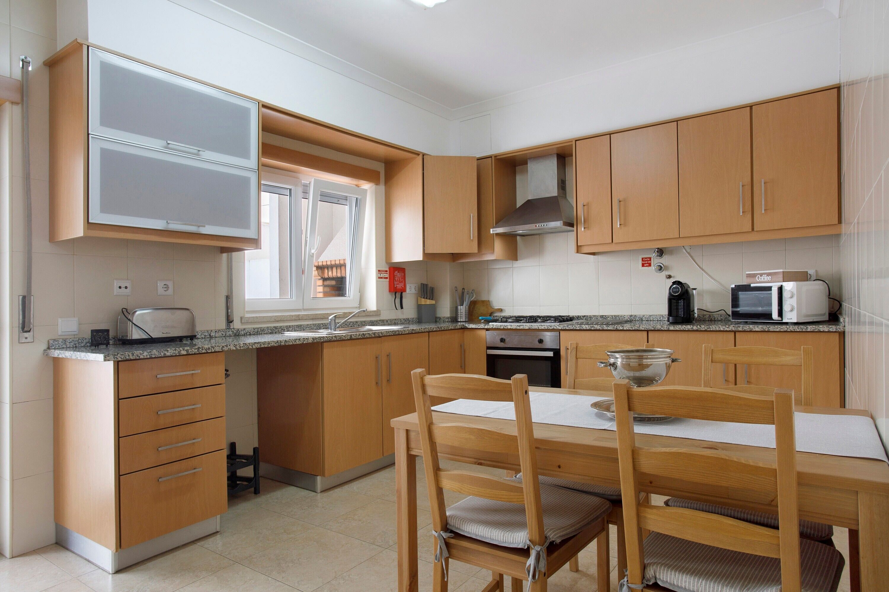 A compact kitchen with wooden cabinets, a built-in microwave, a toaster, and a dining table with chairs.