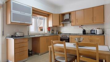 A compact kitchen with wooden cabinets, a built-in microwave, a toaster, and a dining table with chairs.