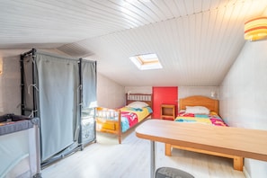 Quarto compacto com duas camas, uma mesinha, uma janela e um claraboia.
