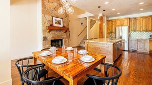 A dining area with a wooden table set for four, surrounded by black chairs. A stone wall and a fireplace are visible in the background. - Charming Mountain Escape Near All the Action (Park City)