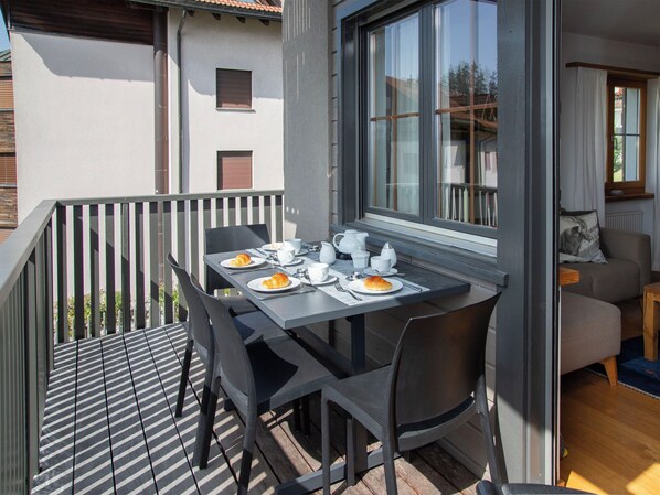 A balcony with a table set for breakfast, including croissants and coffee cups, and a sofa in the background.