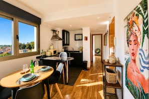 A modern kitchen with a dining area, a view through large windows, and a painting on the wall.
