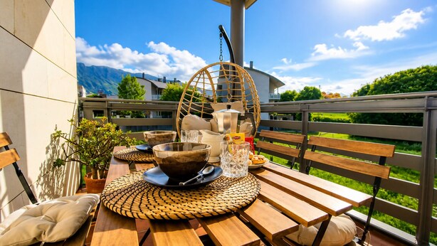 A wooden table with a woven placemat, a bowl, a glass, and a kettle on a balcony with a view of greenery and mountains. - Las Xanas - Views, Swimming Pool and Terrace in LLanes (Llanes)