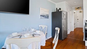 Un coin repas avec une table dressée pour quatre personnes, des chaises blanches, un réfrigérateur noir et un tableau accroché au mur.