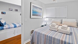 Une chambre à coucher avec un lit, une table de chevet, un tableau accroché au mur et un ventilateur de plafond.