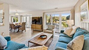 A modern living room with a sofa, coffee table, TV, and dining area with chairs and a table.