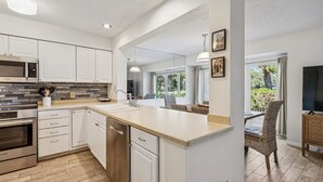 A modern kitchen with white cabinets, a large island, stainless steel appliances, and a dining area with wicker chairs.