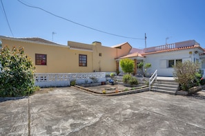 Zona residencial con un patio empedrado, cerca blanca y una escalera que lleva a un edificio con tejado de tejas.