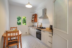 A kitchen with a dining table, chairs, a stove, oven, and a window with blinds.