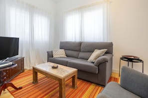 Una sala de estar con un sofá gris, una mesa de centro de madera, un televisor y una pequeña mesita auxiliar.