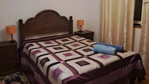 Un dormitorio con una cama de madera, una mesita de noche, una lámpara, un ventilador de techo y una ventana con cortinas.
