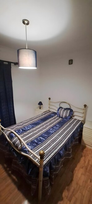 A single bed with a striped bedspread, a bedside table with a lamp, and a hanging light fixture.
