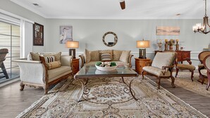 A living room with a glass coffee table, two sofas, a chandelier, and a ceiling fan.