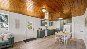 A modern kitchen with wooden ceiling, white cabinets, and a dining area with a table and chairs.