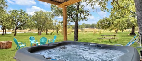 A hot tub with a wooden pergola overhead, surrounded by green grass and trees.