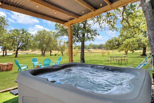 A hot tub with a wooden pergola overhead, surrounded by green grass and trees.