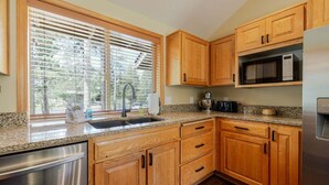Una cocina con armarios de madera, lavavajillas de acero inoxidable, microondas y encimera de granito.
