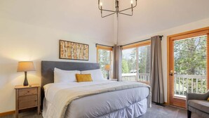 Un dormitorio con cama, mesita de noche, lámpara y vistas al exterior.