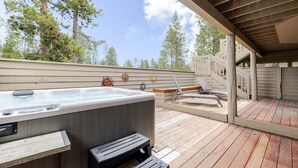Terraza de madera con jacuzzi, sillones de descanso y un espacio cubierto con barandilla.