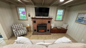 A cozy living room with a fireplace, a plaid armchair, and a sofa with striped cushions.