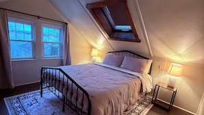 A bedroom with a sloped ceiling, a skylight, a bed with a headboard, two bedside lamps, and a patterned rug.