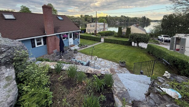 A residential area with a house, a stone staircase, a lawn, and a lake in the background.