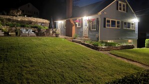 A house with a well-maintained lawn, a stone retaining wall, and a patio with outdoor furniture.