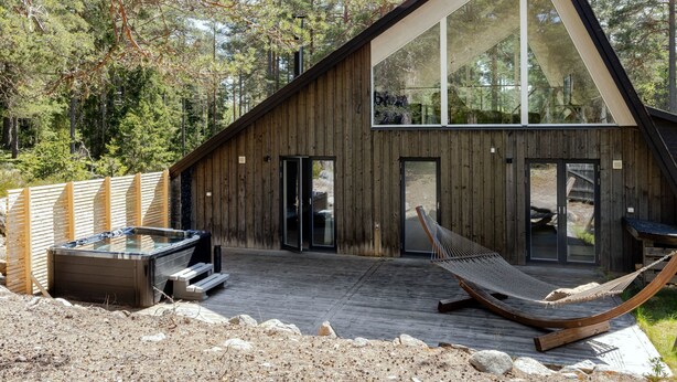 A modern wooden cabin with a hot tub, hammock, and glass doors.