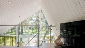 A modern interior with a large TV, a wooden floor, and a view of a forest through large windows.