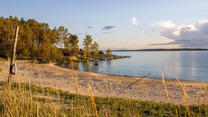 A beach with a clear view of the water, a sandy shore, and a forest in the background.