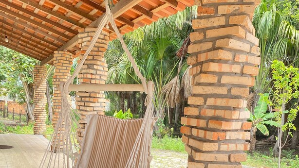 A covered outdoor area with a hanging hammock chair, brick pillars, and a tiled floor.