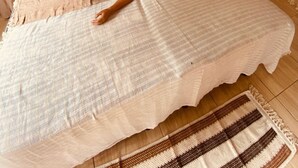 A person lying on a bed in a room with a hammock, a wall hanging, and a patterned rug.