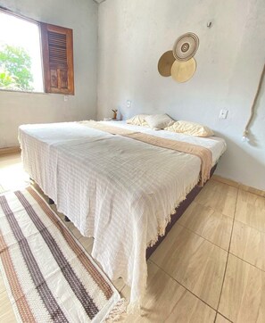 Une chambre avec deux lits, une grande fenêtre, une assiette décorative accrochée au mur et un tapis tissé.
