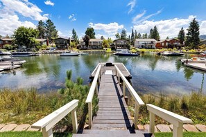 A wooden dock leading to a calm lake with boats, surrounded by houses and greenery. - Waterfront Family Home with Private Boat Dock (South Lake Tahoe)