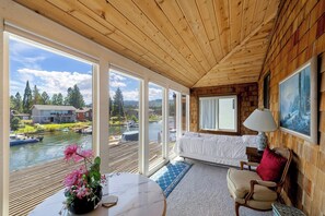 A room with a bed, a table with a vase, and a view of a lake and houses. - Waterfront Family Home with Private Boat Dock (South Lake Tahoe)