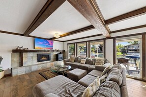 A living room with a fireplace, a large sectional sofa, a glass coffee table, and a television mounted on the wall. - Waterfront Family Home with Private Boat Dock (South Lake Tahoe)