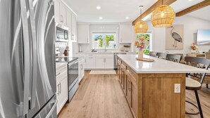 Una cocina moderna con electrodomésticos de acero inoxidable, armarios blancos, una isla de madera e iluminación colgante.