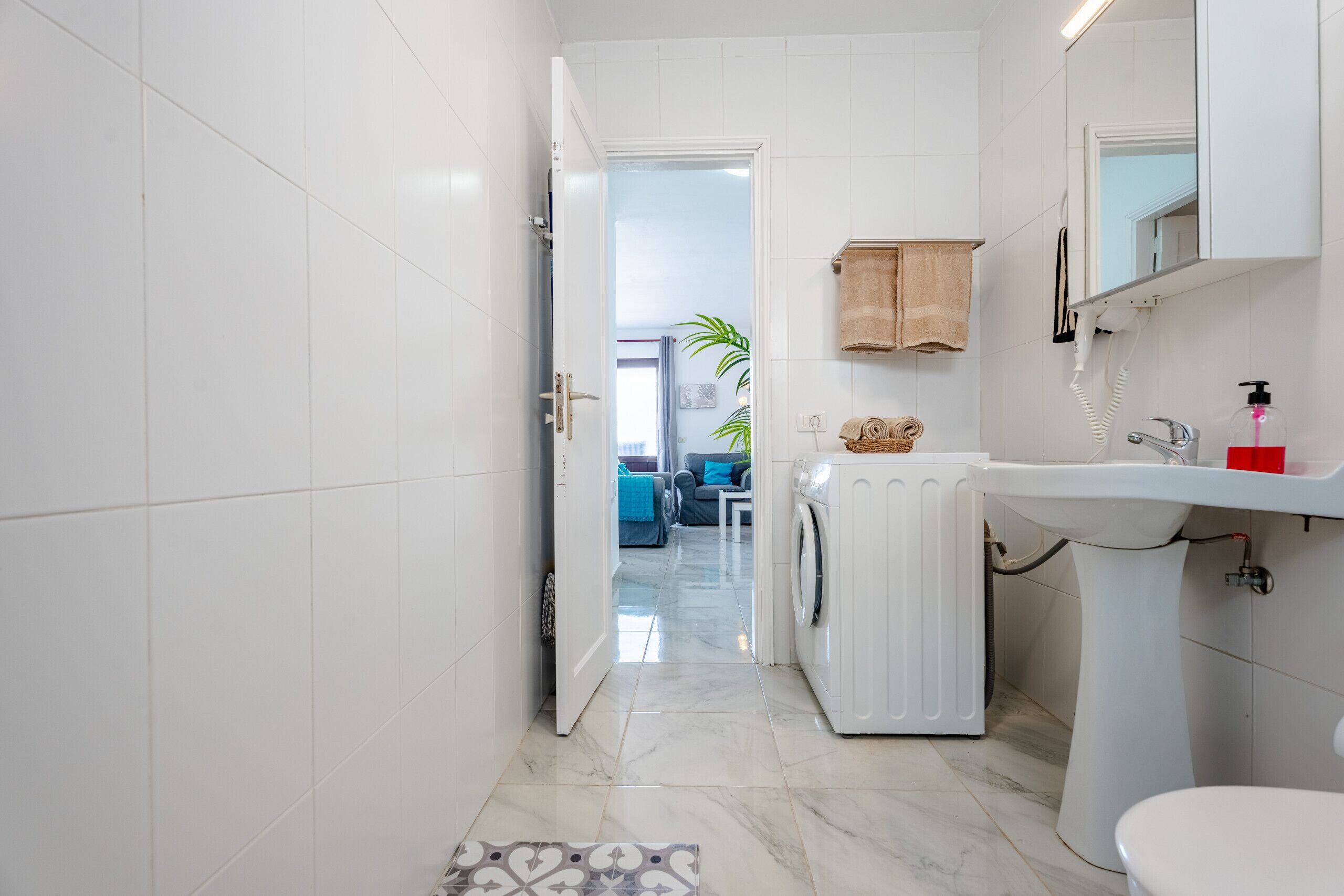 A modern bathroom with a white sink, a mirror, and a washing machine.