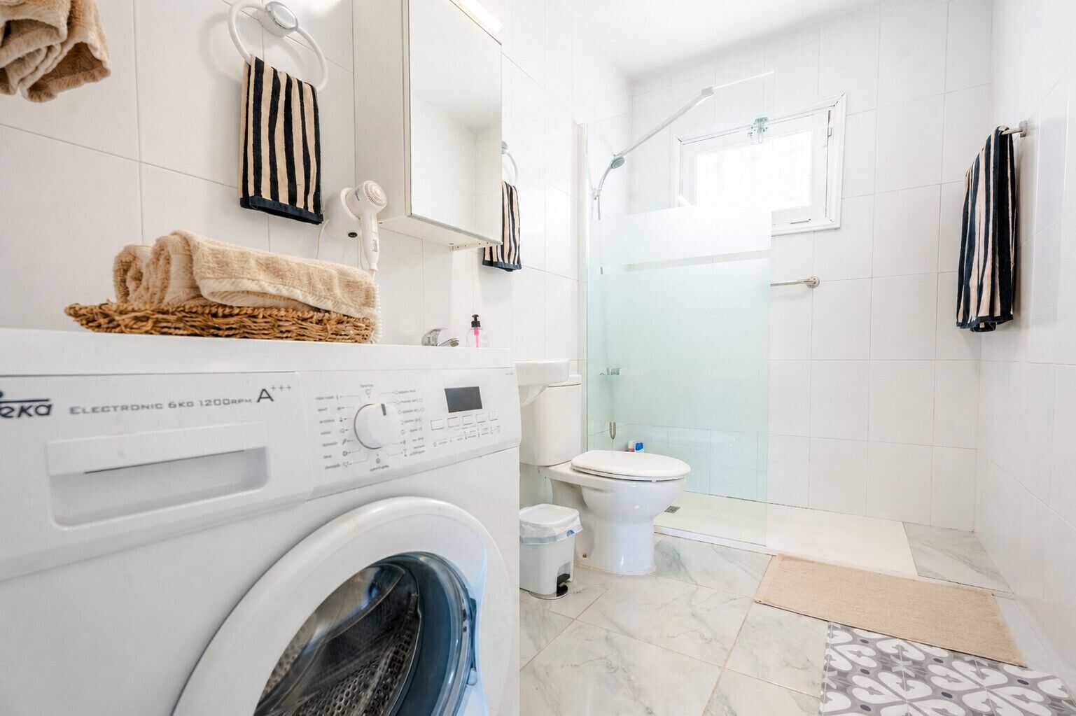 Un baño moderno con lavadora, inodoro, cabina de ducha con mampara de vidrio y toallas a rayas.