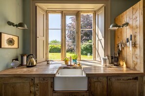 A kitchen with a large window, wooden cabinets, and various kitchen items on the counter. - Manor Farm - Gorgeous House in Somerset (Shepton Mallet)