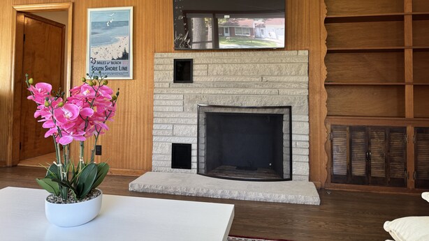 A living room with a stone fireplace, wooden paneling, a television mounted above it, and a poster on the wall.