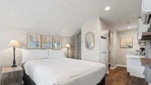 Habitación de hotel con una cama grande, lámparas de noche, una mesita, un espejo y una kitchenette.