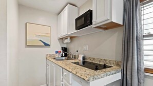 Una cocina compacta con armarios blancos, encimera de granito, microondas, lavabo y un cuadro en la pared.